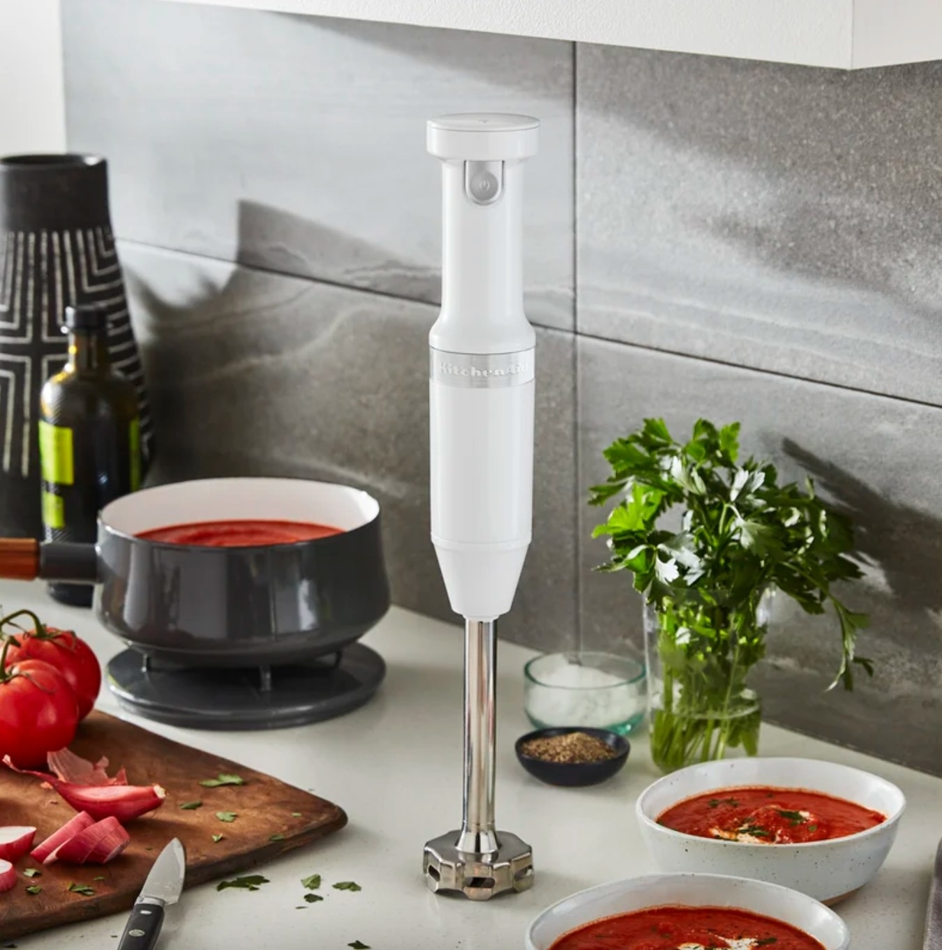 the white cordless hand blender on a counter with bowls of tomato soup