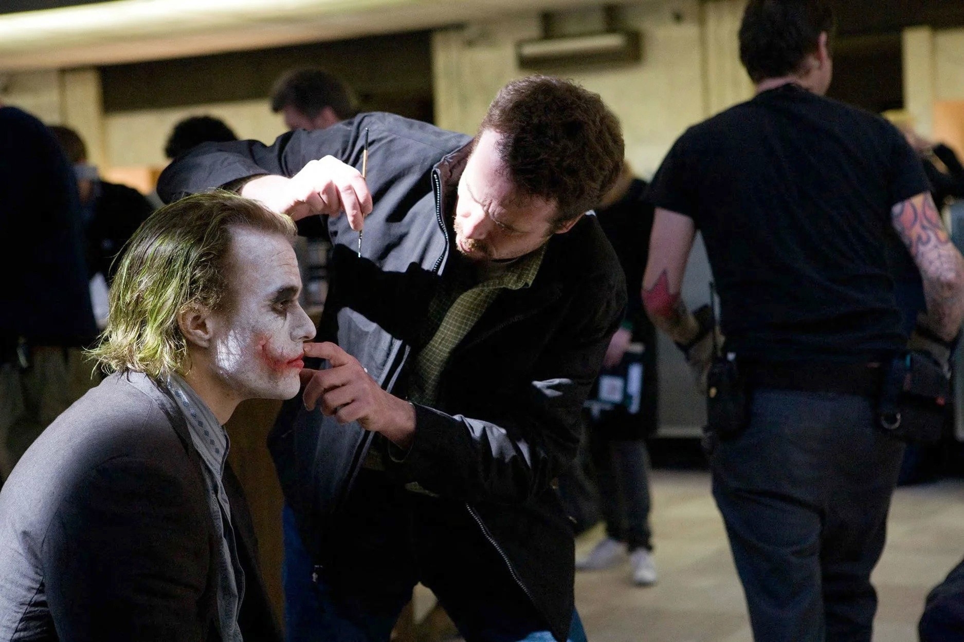 A man applies makeup to the joker on set