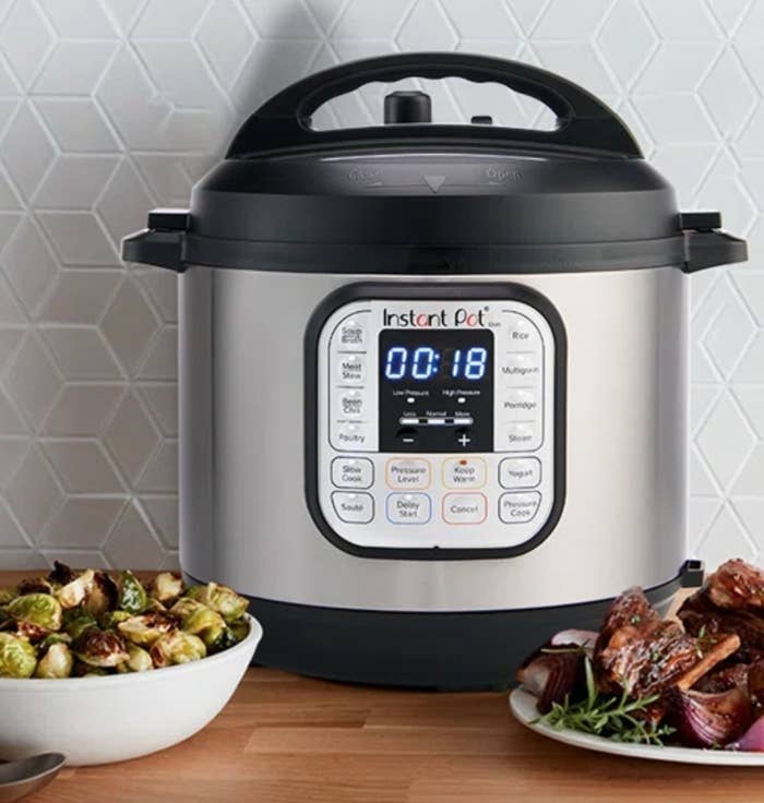 the silver pressure cooker on a counter with bowls of brussels sprouts and meat