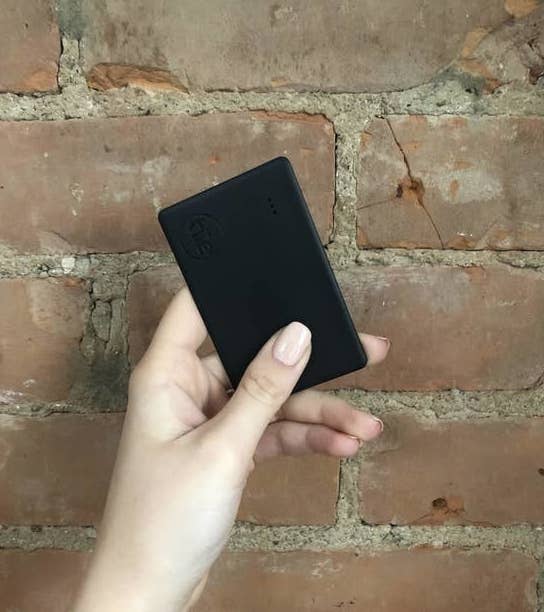 a person holding the tile slim in front of a brick wall