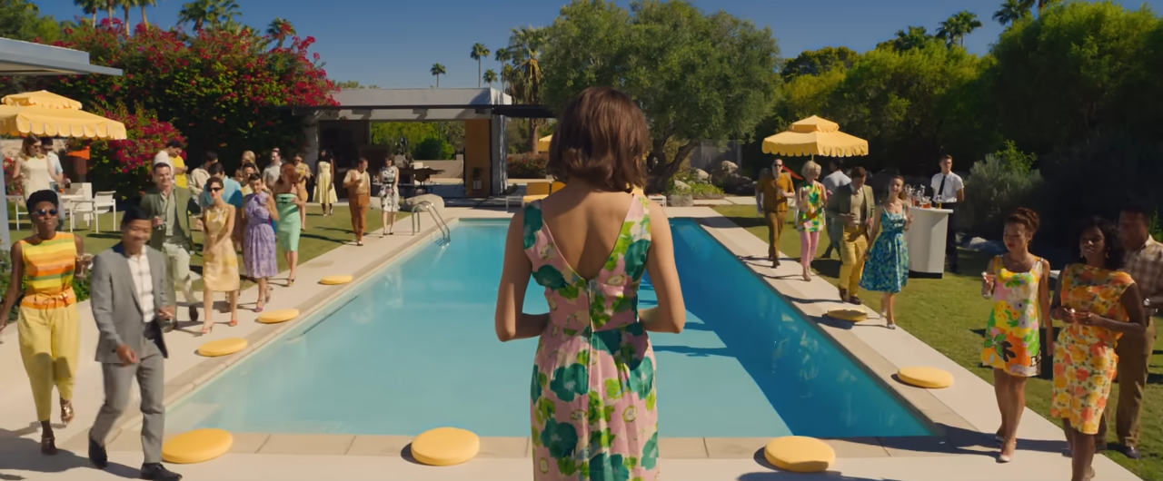 A view from behind a woman as she stands in front of a pool and several people look at her