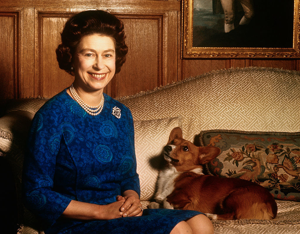 Queen Elizabeth II smiling and a corgi looking up at her