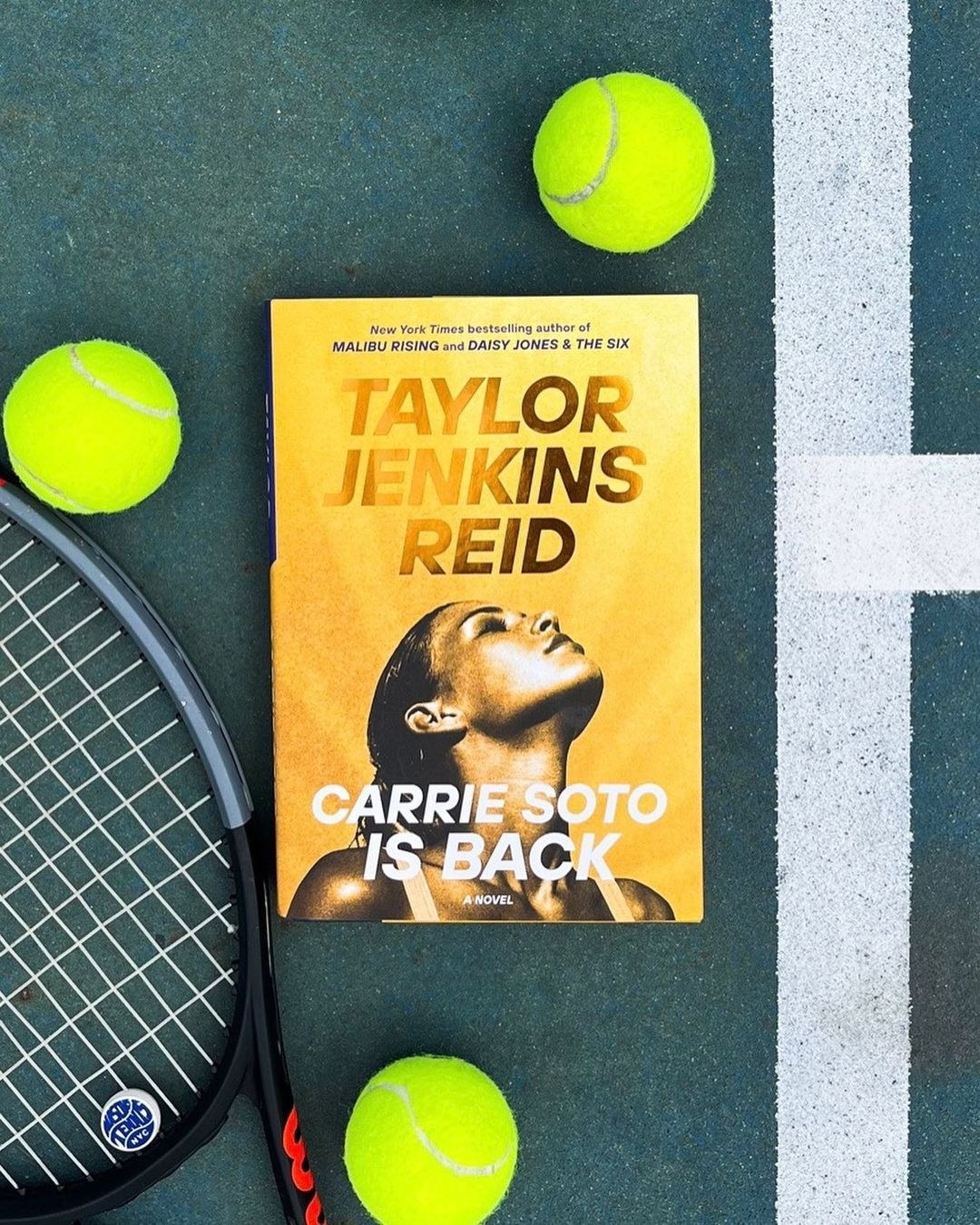 The book on a tennis court surrounded by rackets and balls
