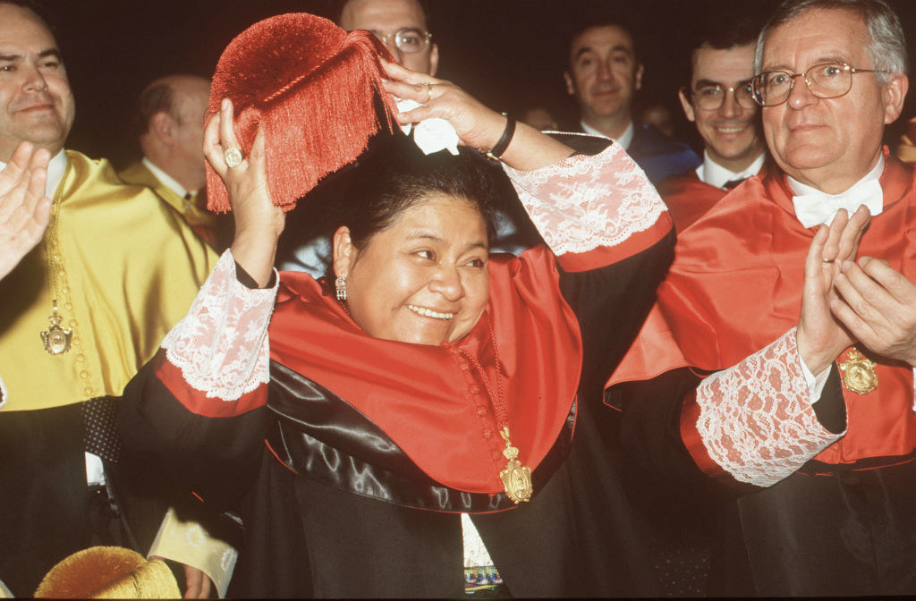 Menchú waving and smiling and wearing a robe