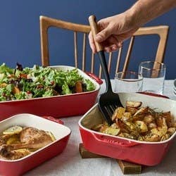 three red Staub bakeware pans filled with salad and baked chicken and potatoes