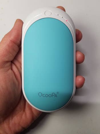 a reviewer holding the palm-sized, oval-shaped blue warmer