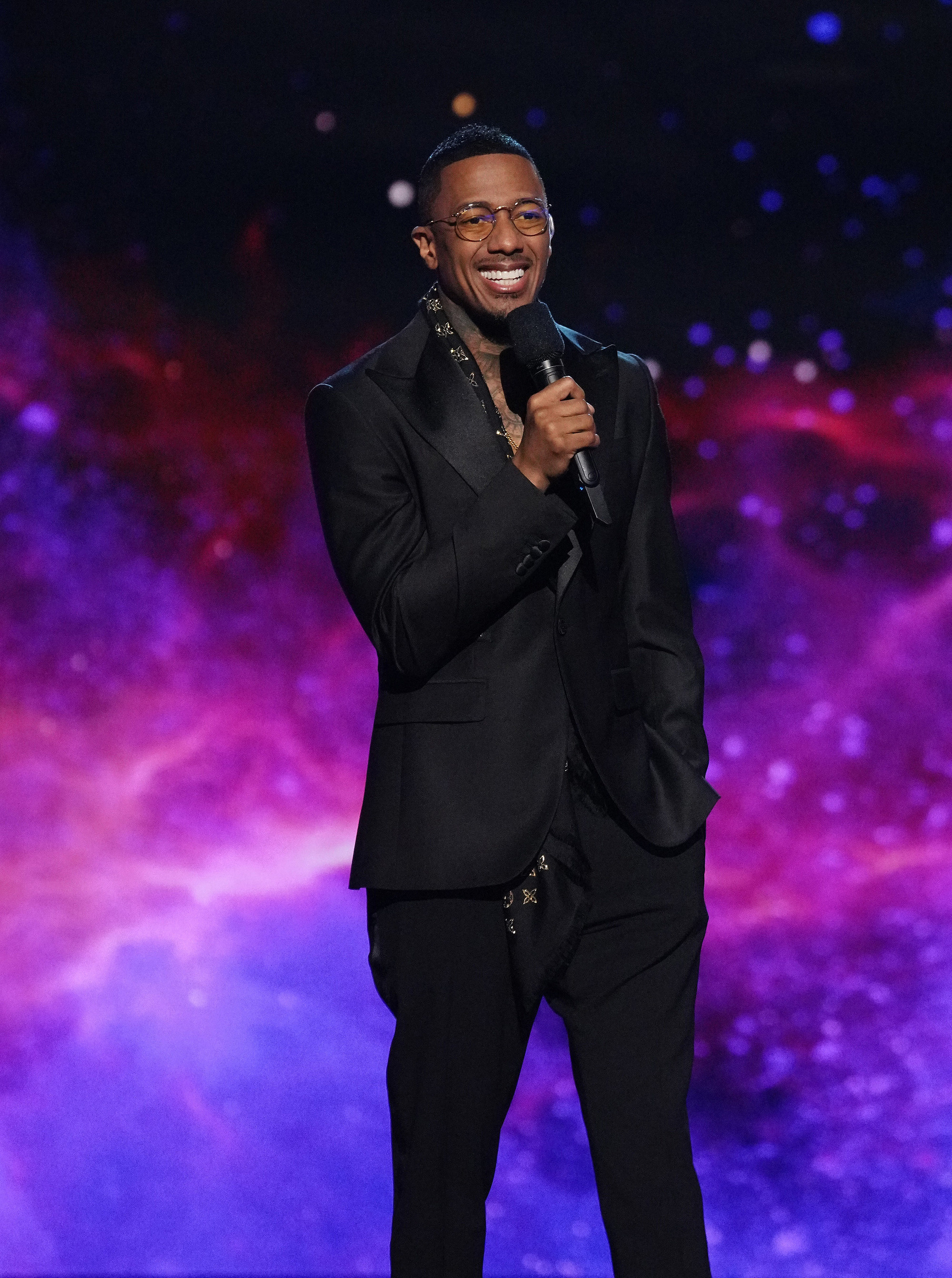 Nick Cannon smiling and holding a mic onstage