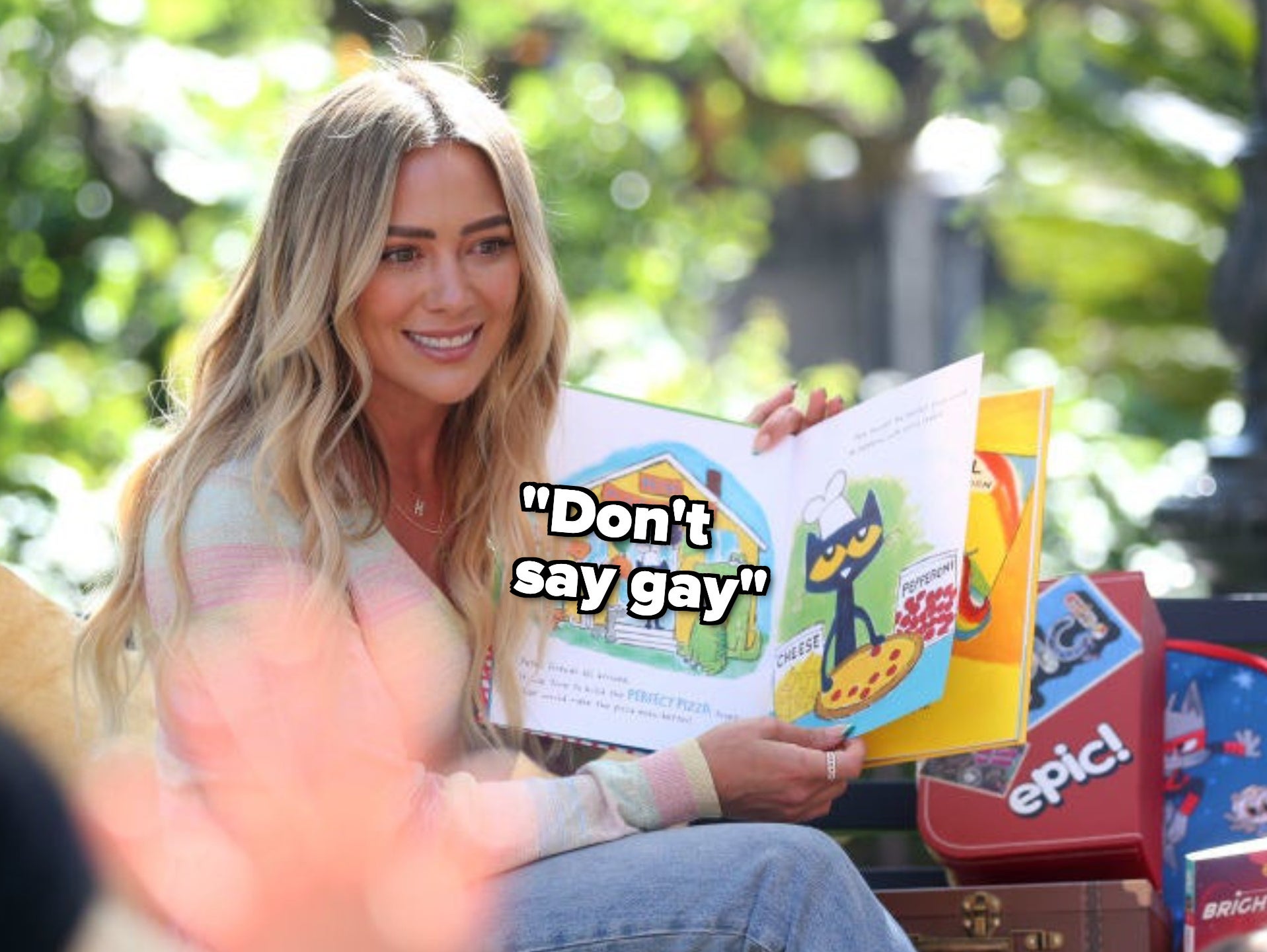 Hilary smiling and sitting with an open children&#x27;s book with the caption &quot;Don&#x27;t say gay&quot;