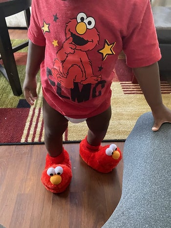 reviewer's photo of their child wearing the Elmo slippers