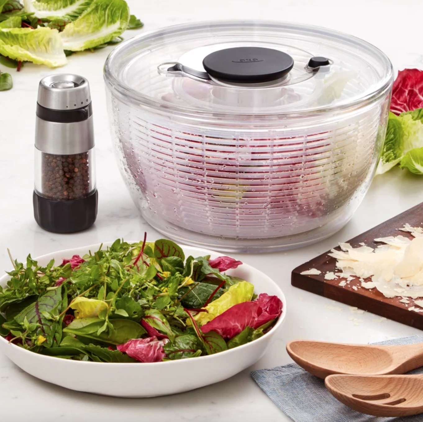 the white salad spinner on a counter with a salad and ingredients