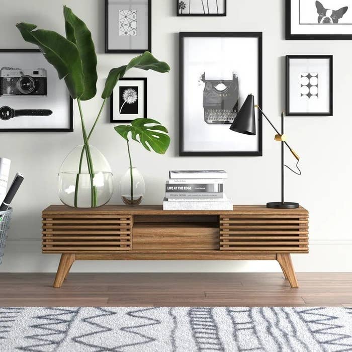 a wood tv stand with plants, books, and a lamp on top