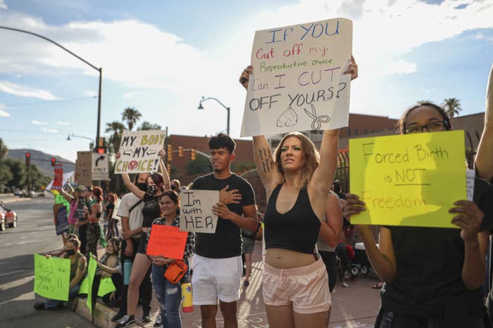 People stand and sit on the sidewalk holding signs