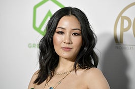Constance Wu wears a strapless green dress with layered gold necklaces with blue gems.