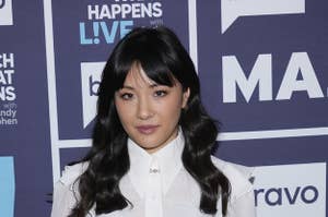 Constance Wu wears a cropped white button-up top with black pants with her hair in waves.