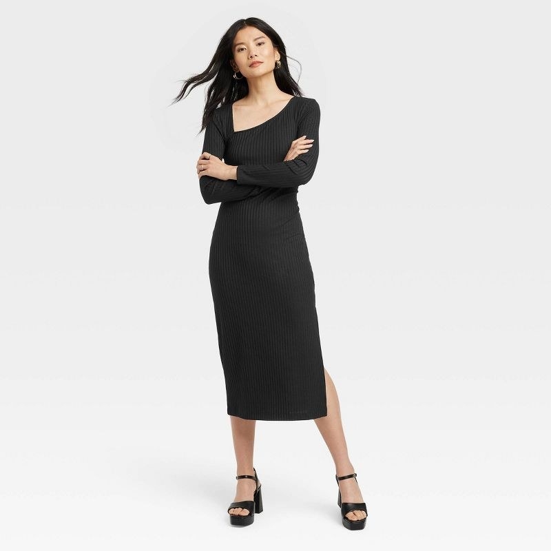 model in black ribbed midi dress with an asymmetrical dipped neckline, long sleeves, and a slit.