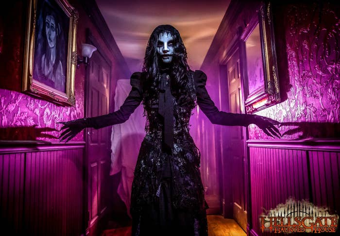 A ghoulish woman in a black dress haunts a purple-soaked hallway at HellsGate Haunted House