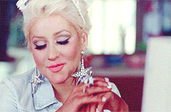 Christina Aguilera sitting at a computer, smiling smugly and clicking a mouse