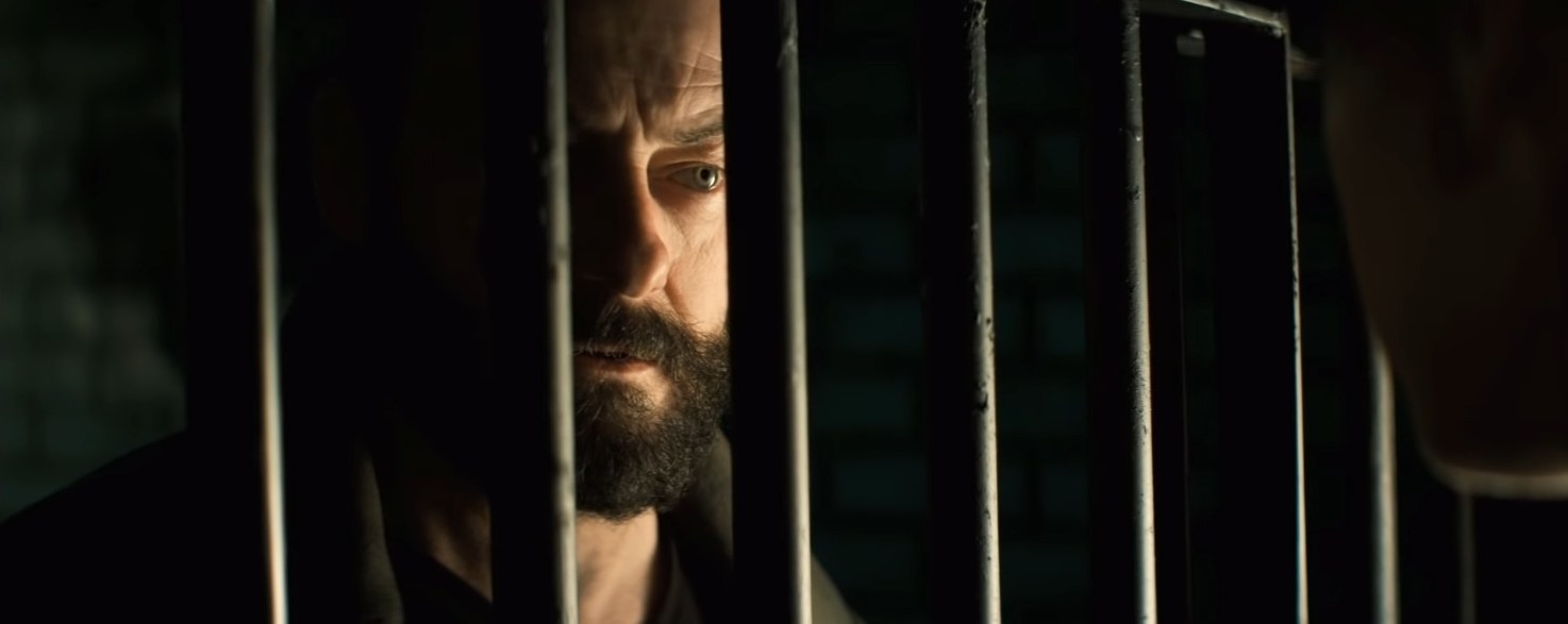 An intense, bearded stranger stares at someone through the eye of a jail cell in &quot;Let Us Prey&quot;