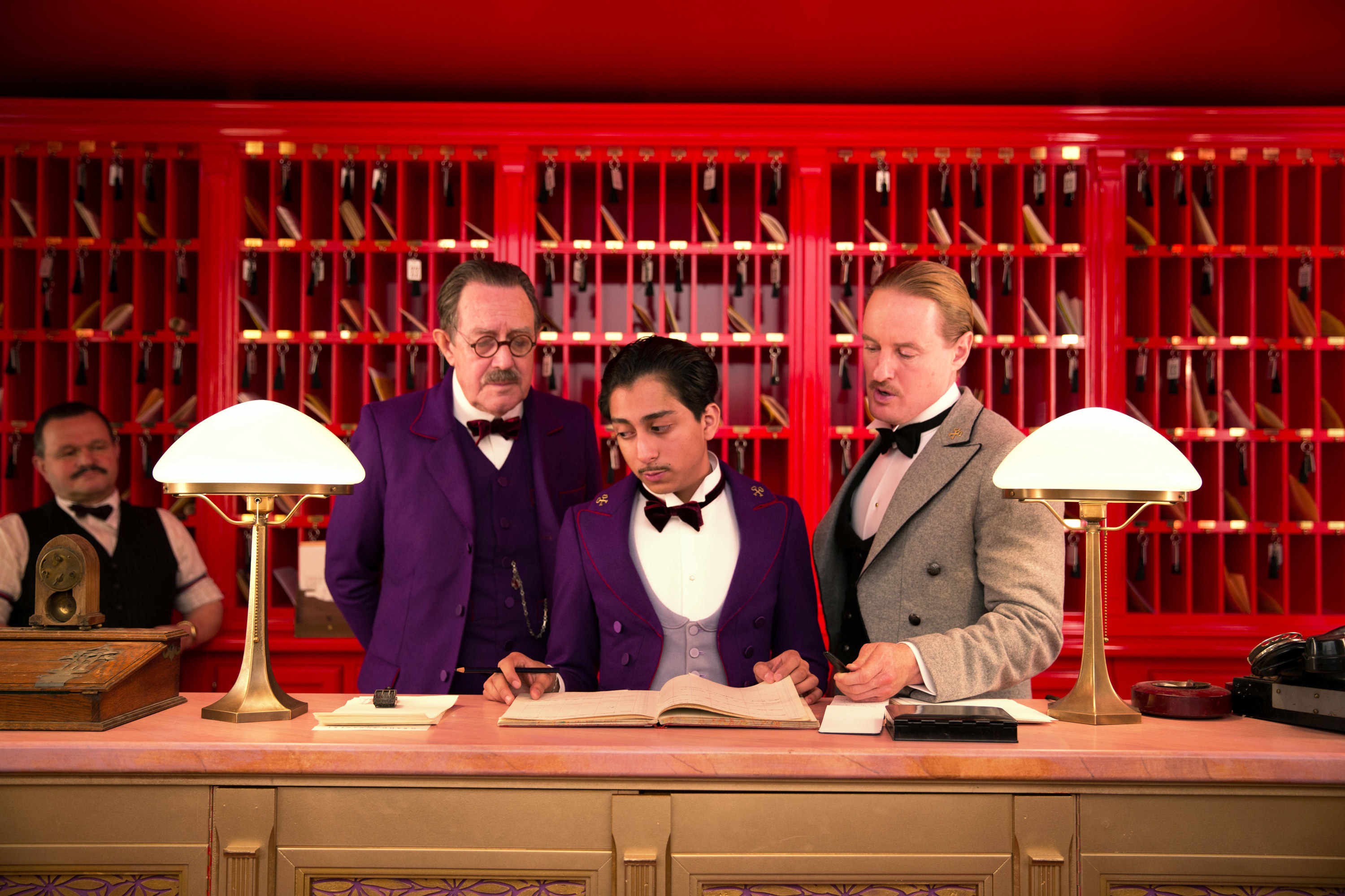 Three men stand at a hotel desk