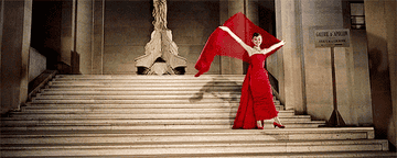 Audrey Hepburn in red dress with white long gloves and matching shawl above her head, descending stairs