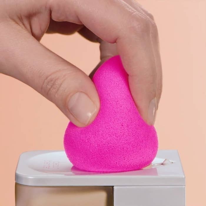 A person tapping a sponge on the top of a foundation bottle