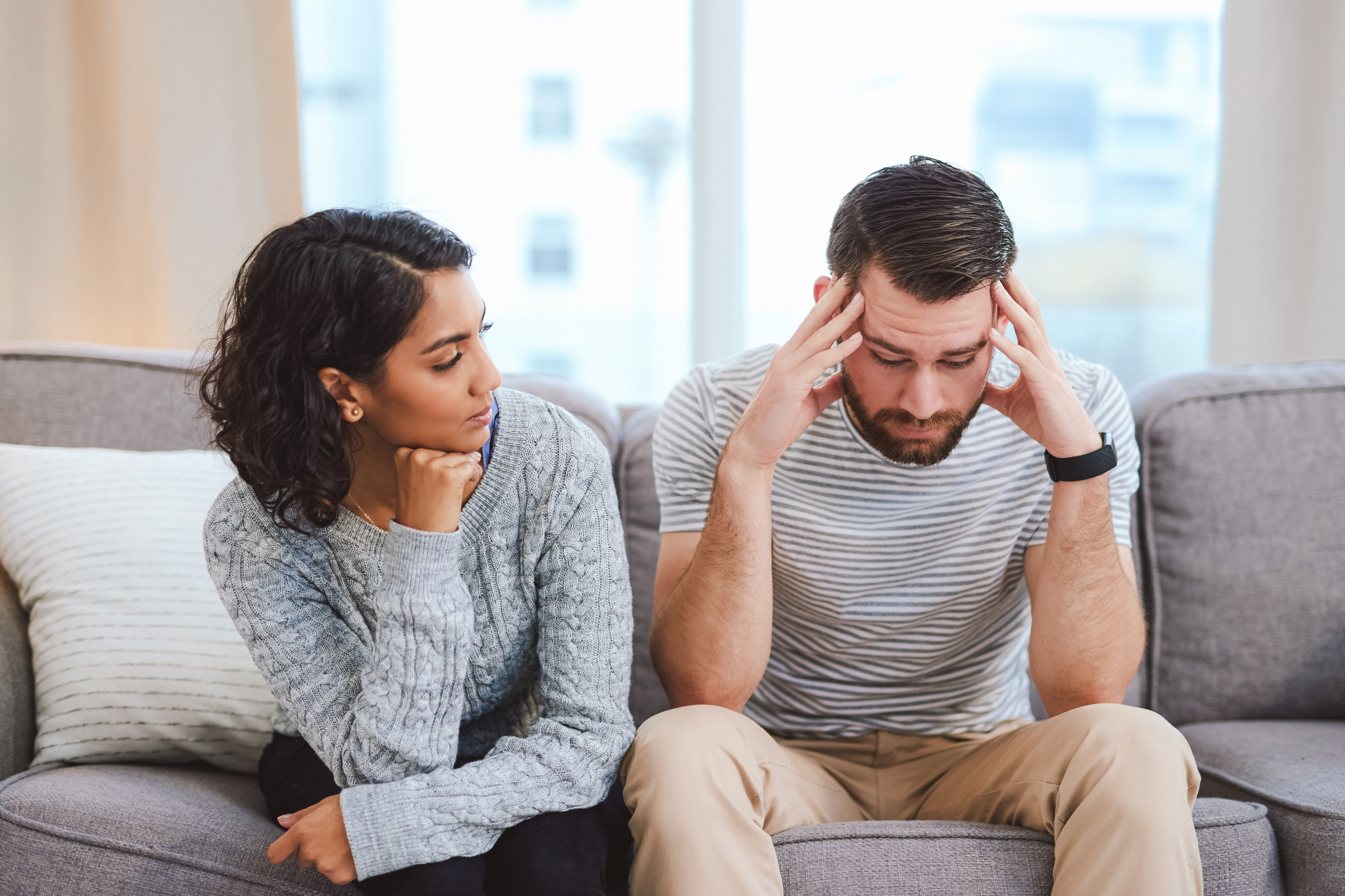 A woman and man sitting on a couch, while he has his head in his hands