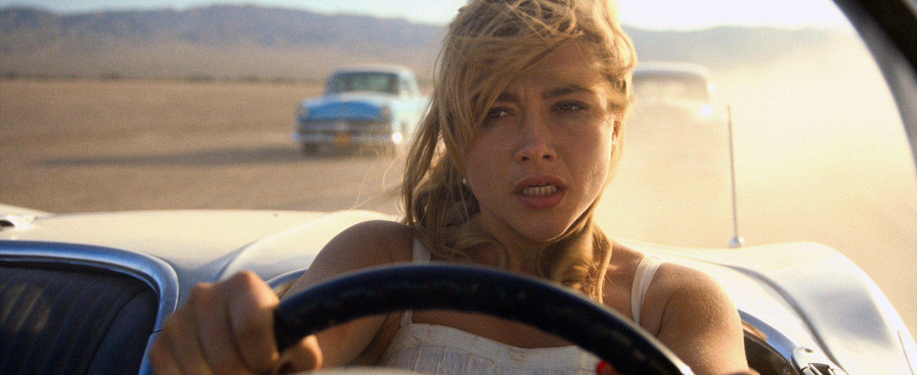 Florence Pugh driving and looking stressed with two cars behind her in a scene from the film