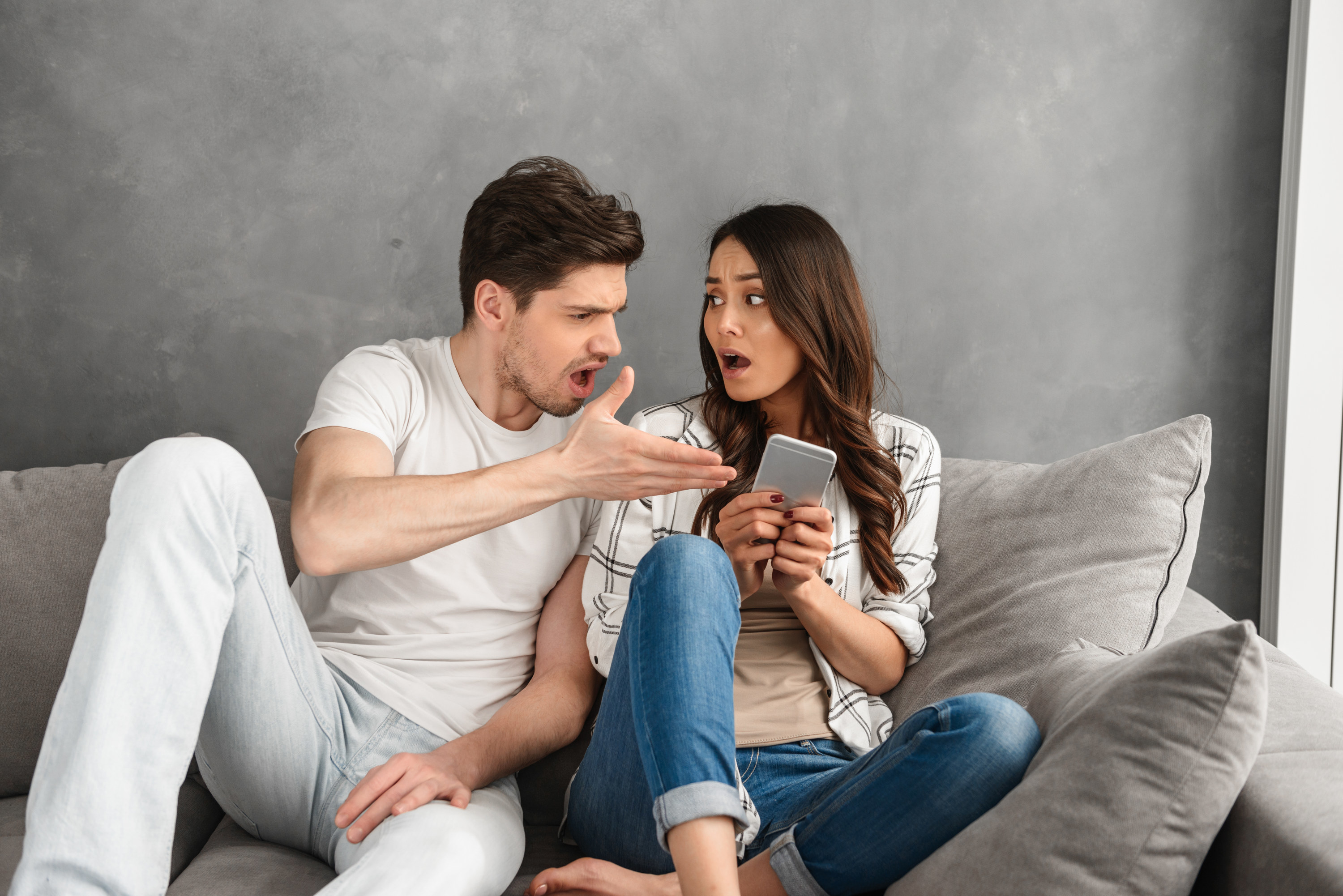 a guy looking appalled and gesturing to a woman&#x27;s phone as she talks as well