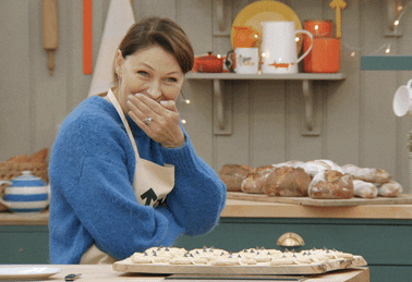 a woman covering her mouth and laughing on a baking show