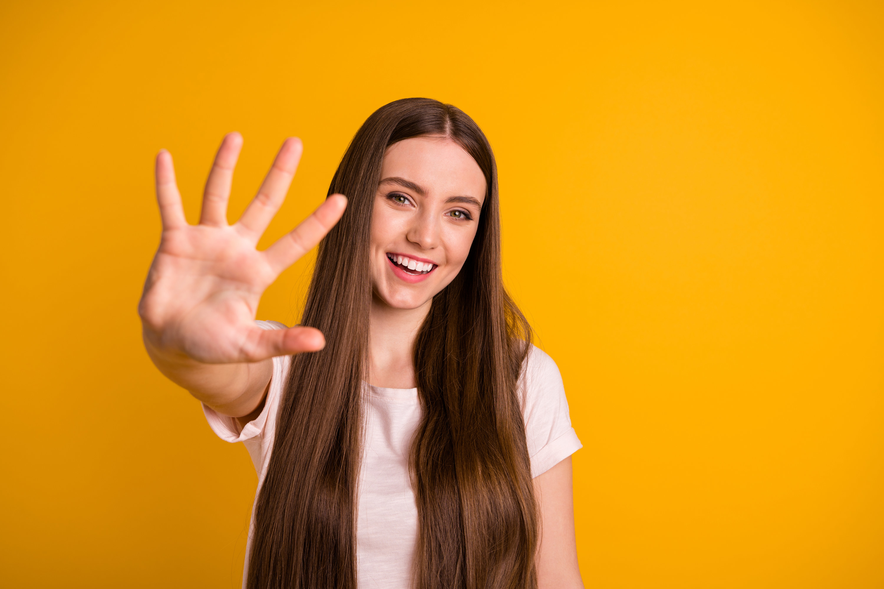 A woman stands against a yellow background and holds up her hand