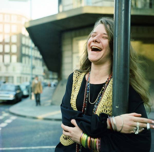Joplin laughing and holding a cigarette on a street corner