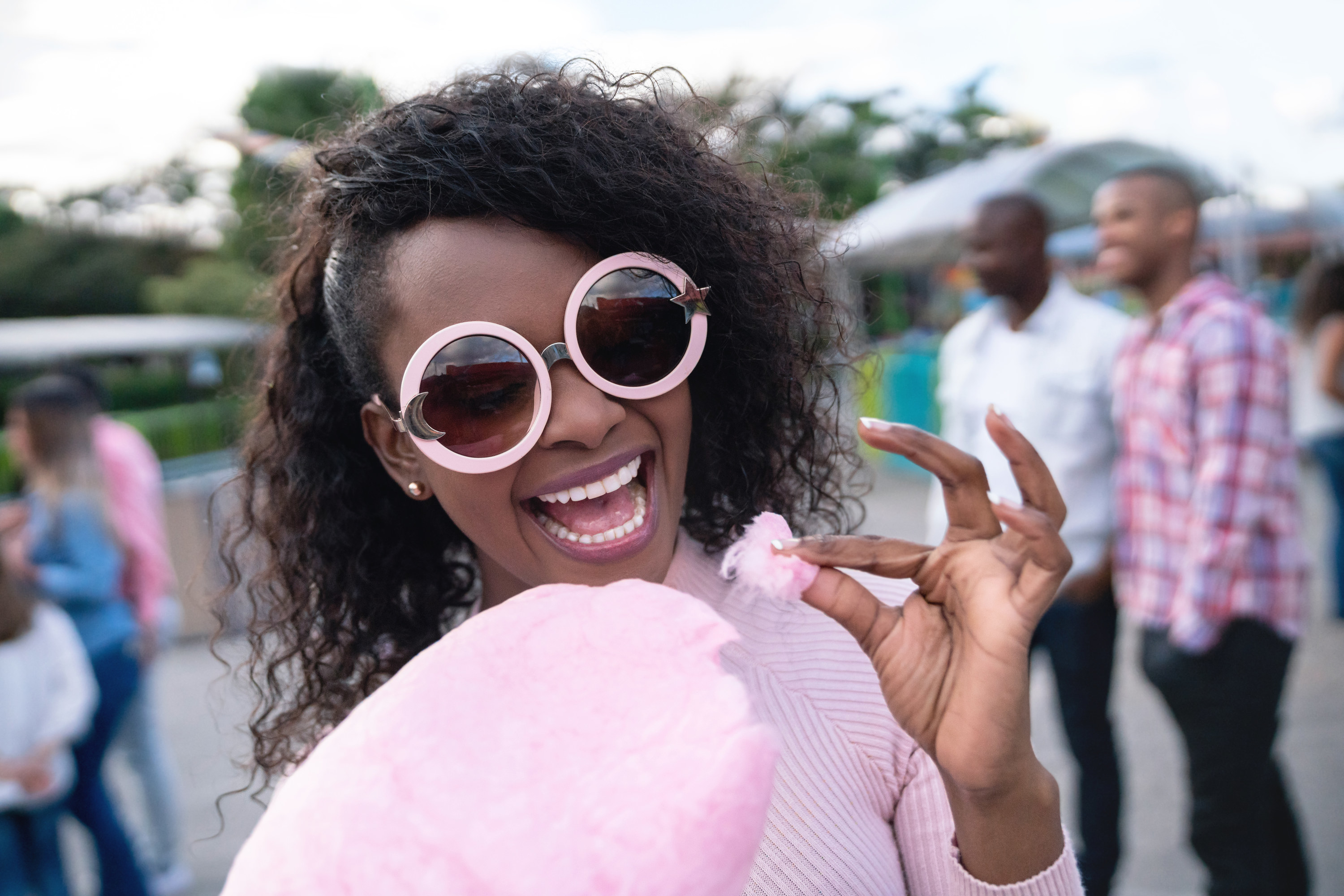 A woman smiles while eating cotton candy at an amusement park