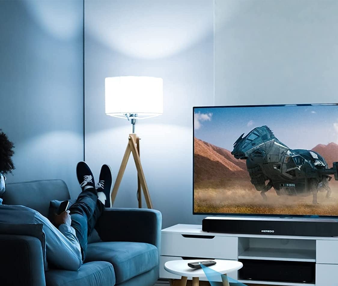 person sitting on a couch watching TV with the sound bar under it