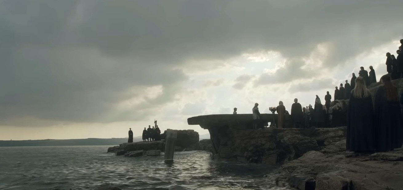 A group of mourners stand on rocks by the sea as the coffin is dropped into the water