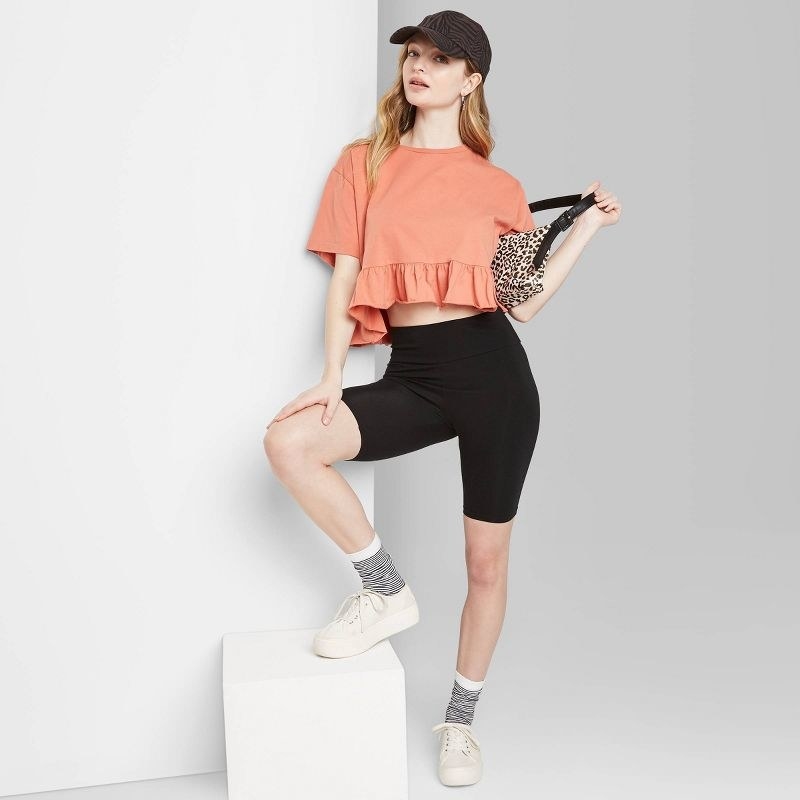 Model wearing black bike shorts with orange shirt and and white sneakers