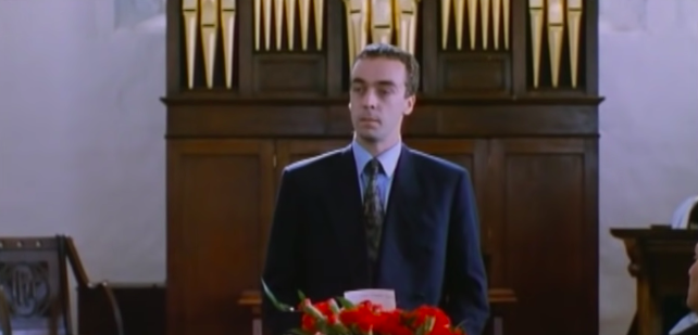 A man stands in front of a casket giving a eulogy