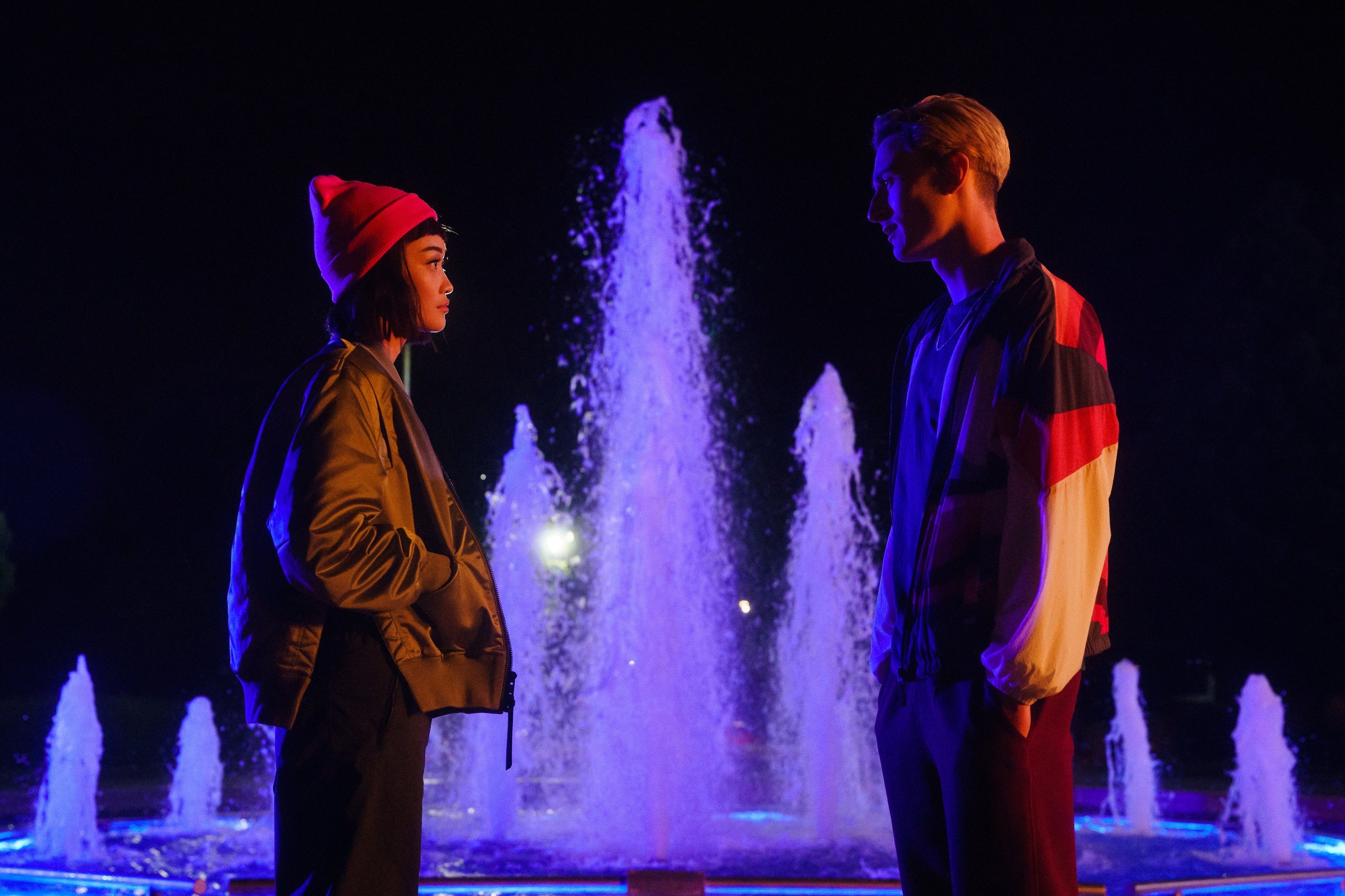 a girl and a guy stare at each other in front of a fountain