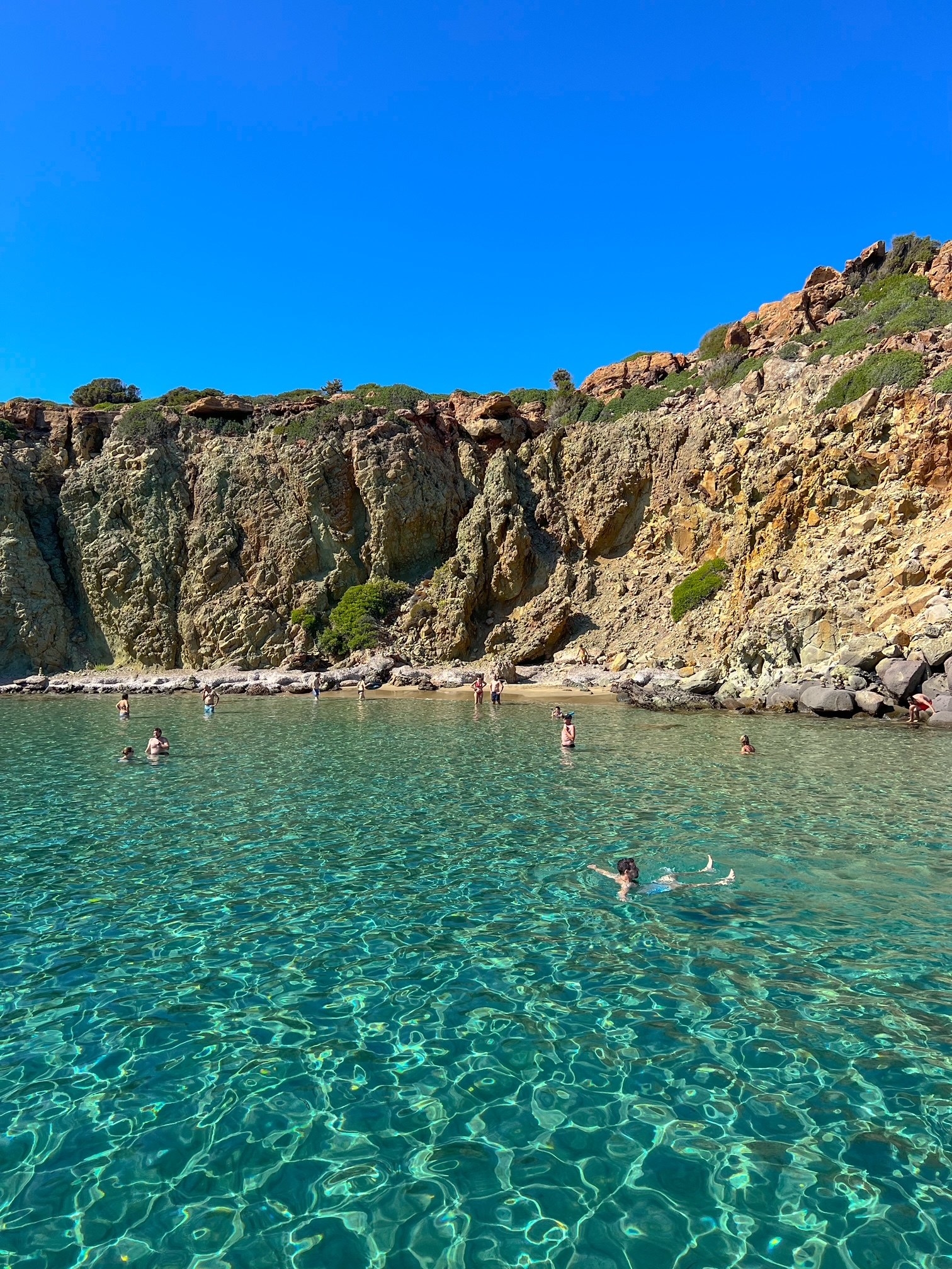 Blue water and people swimming surrounded by cliffs.