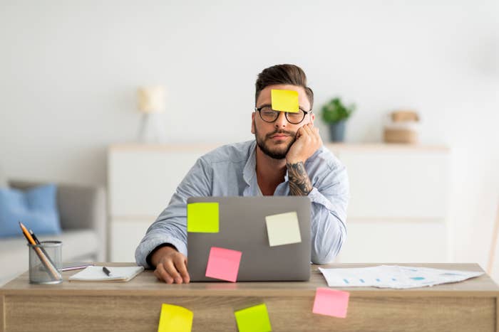tired man at his work desk with multicolored post it notes stuck everywhere