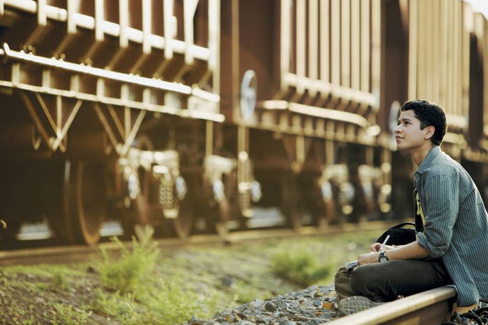Rajat Barmecha sitting on railway tracks cross-legged and writing in a notebook while a cargo train passes by on the parallel track