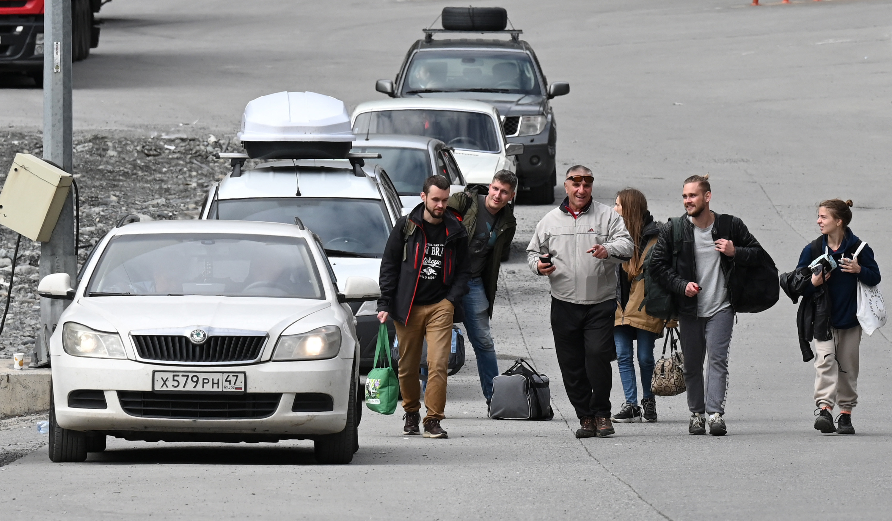 A group of people with luggage walk neck to a line of cars
