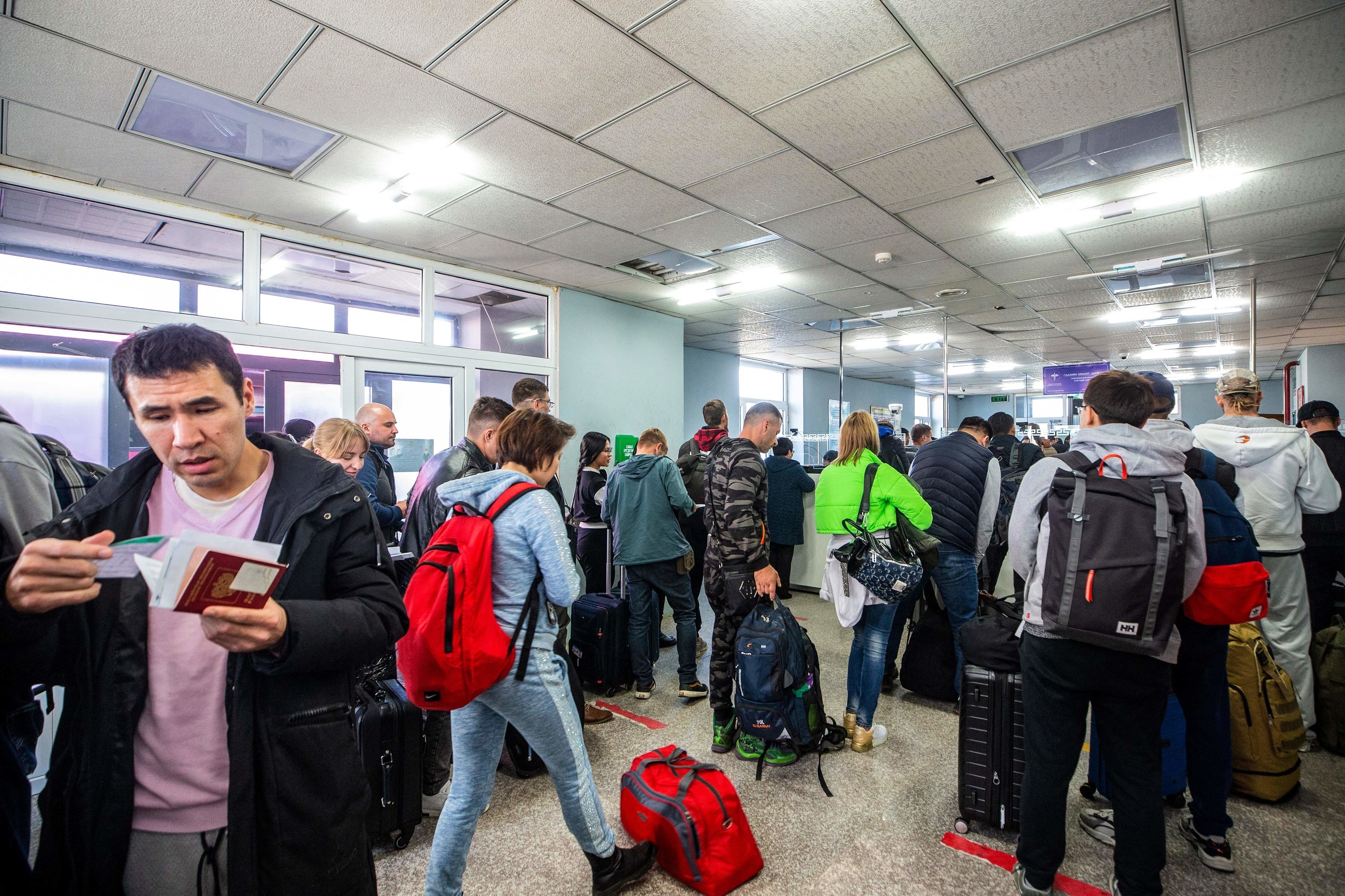 A crowded group of people stand in line with luggage inside a checkpoint facility