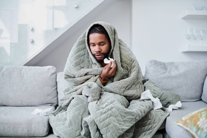 a man covered in a blanket with tissues in his hand