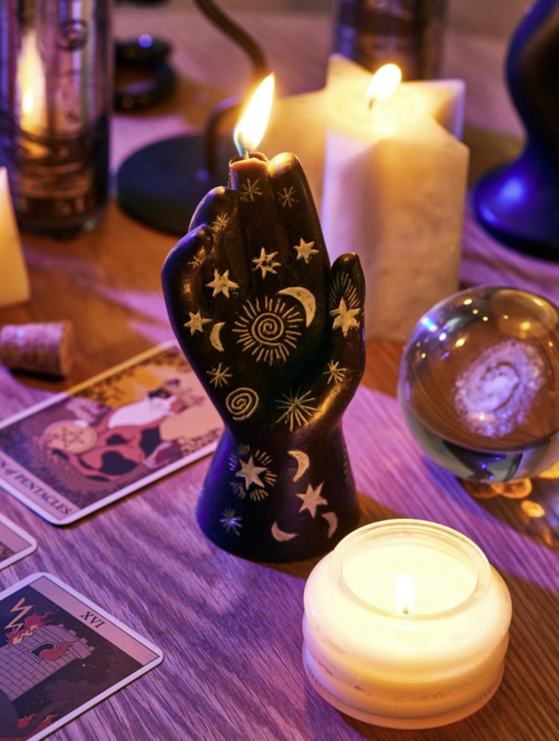 the hand shaped candle on a table next to some tarot cards