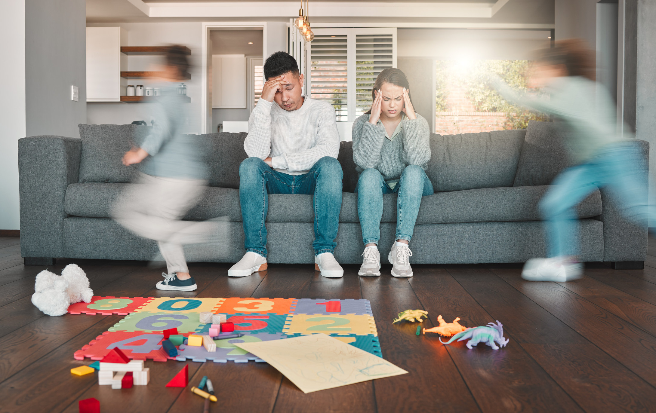 tired parents on couch as kids run around