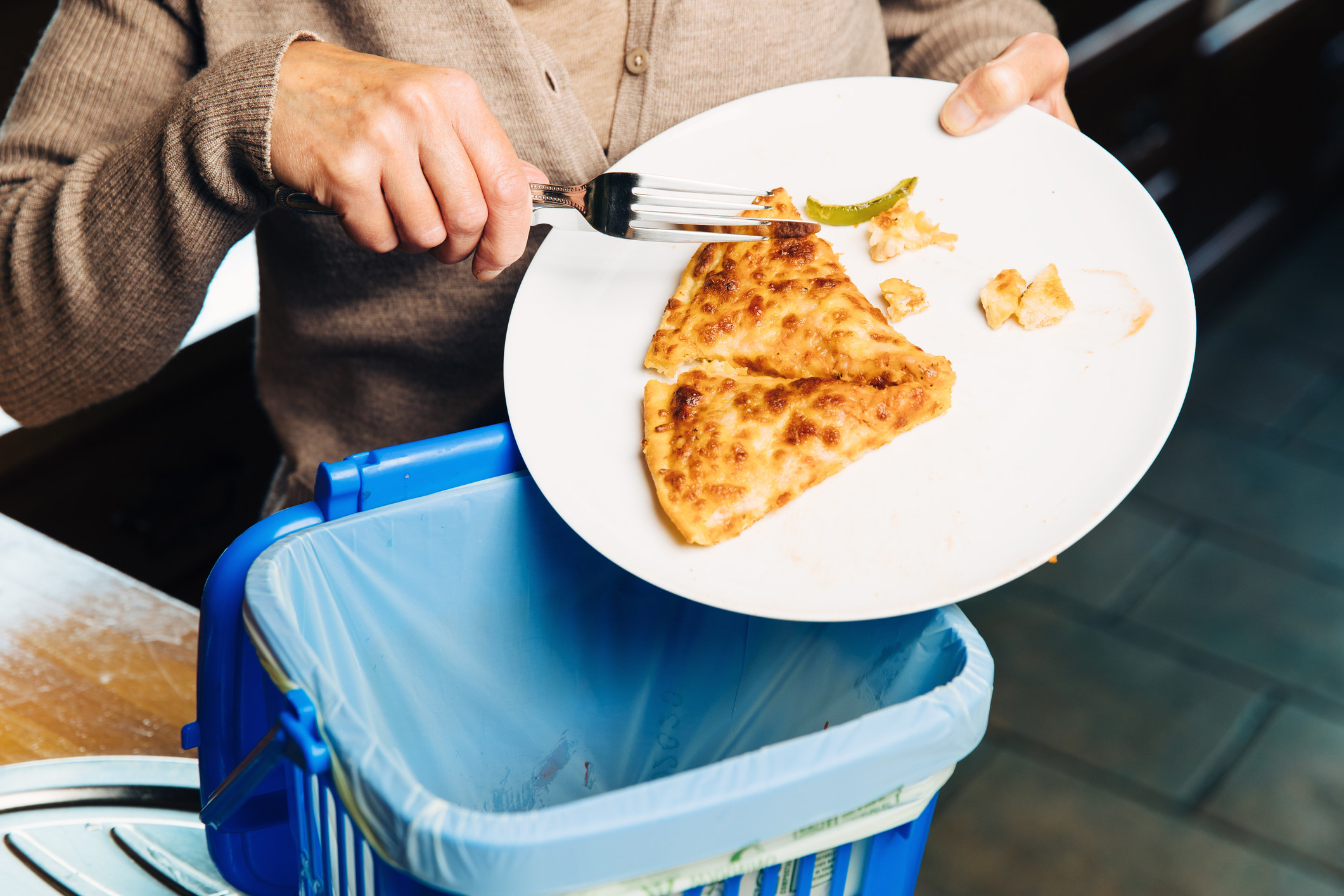 A person throwing pizza in the garbage can