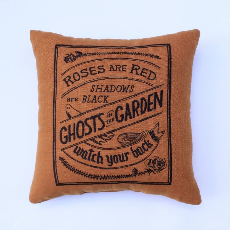 The throw pillow, which reads Roses are Red, Shadows are Black, Ghosts in the Garden, Watch Your Back