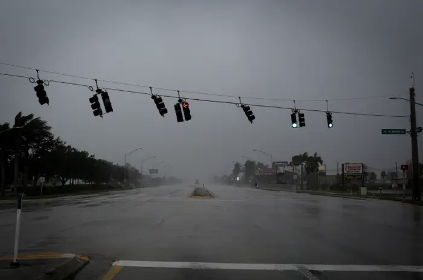 a flooded road, stormy grey skies, a string of traffic lights swaying in intense wind