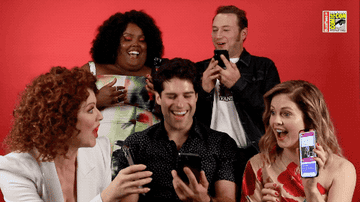 GIF of the cast laughing together and holding their cellphones