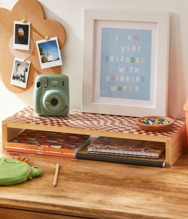 a desk riser on a wood desk with an assortment of decor and office supplies around it